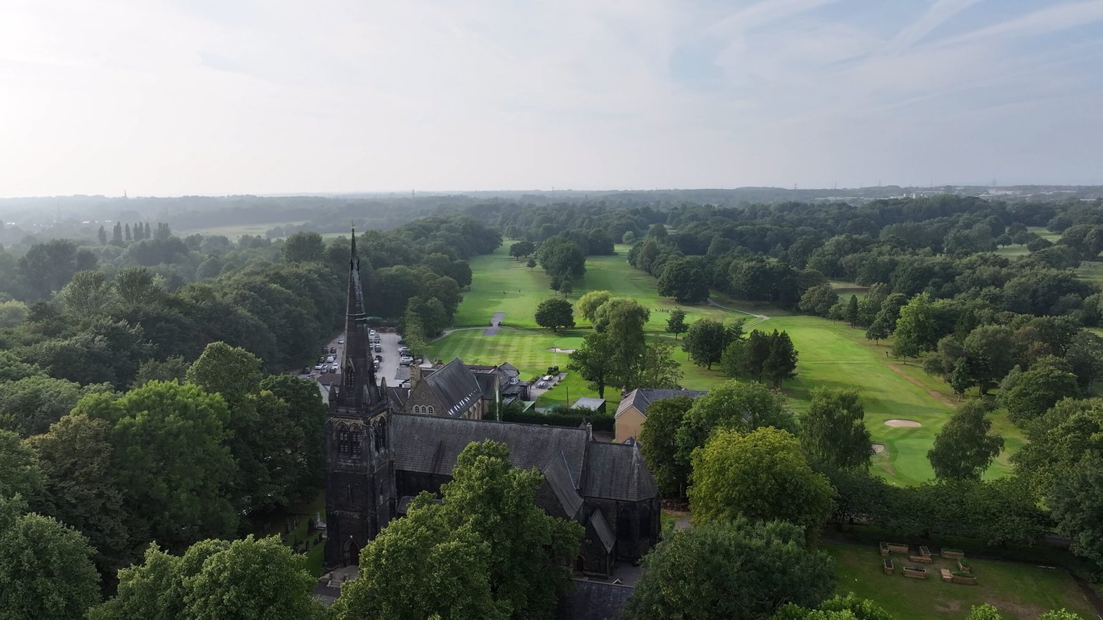 Drone photo of tree-lined fairway and Church at Worsley Golf Club